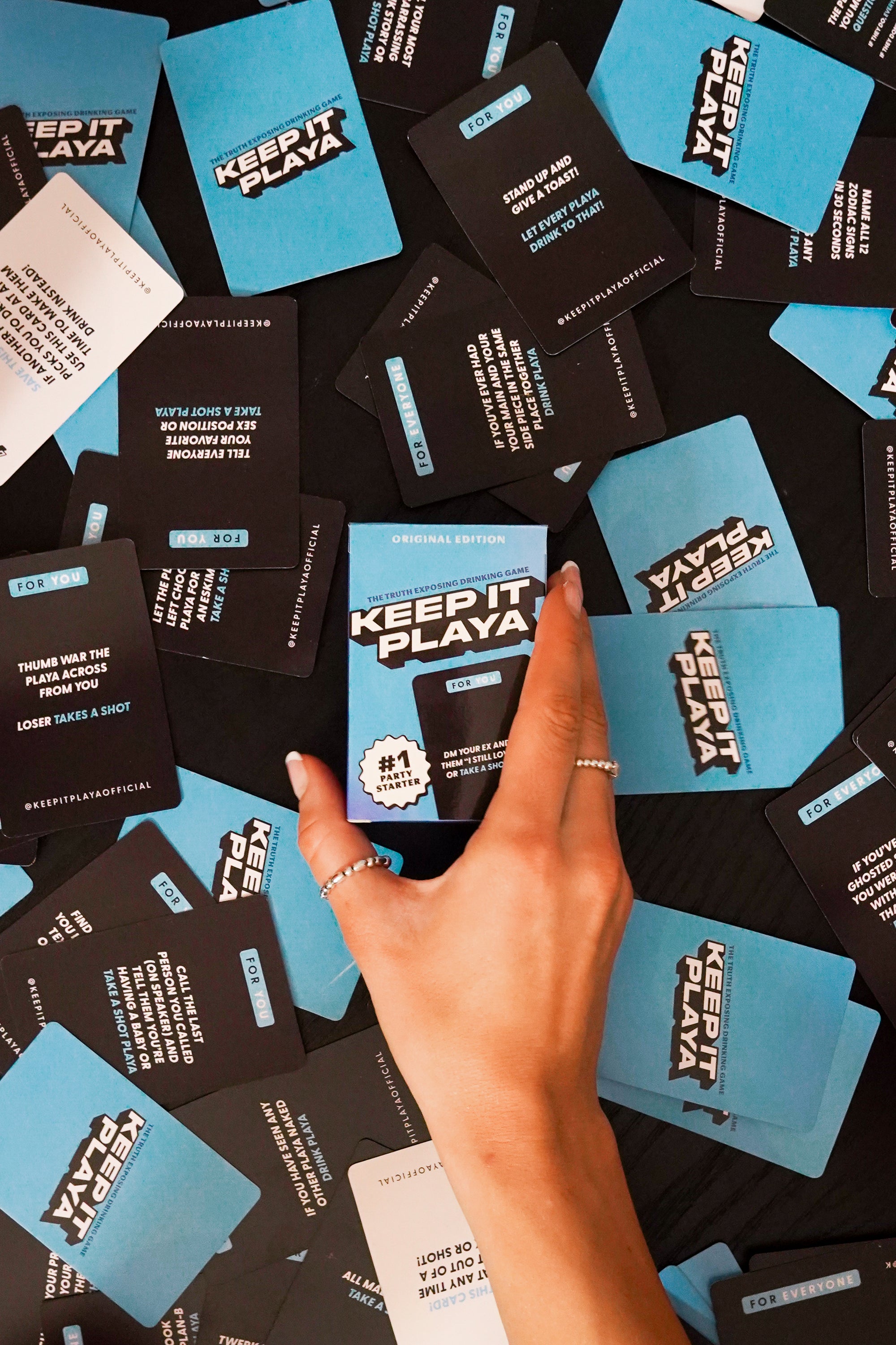 image of hand holding Keep It Playa original edition box with cards spread out on table