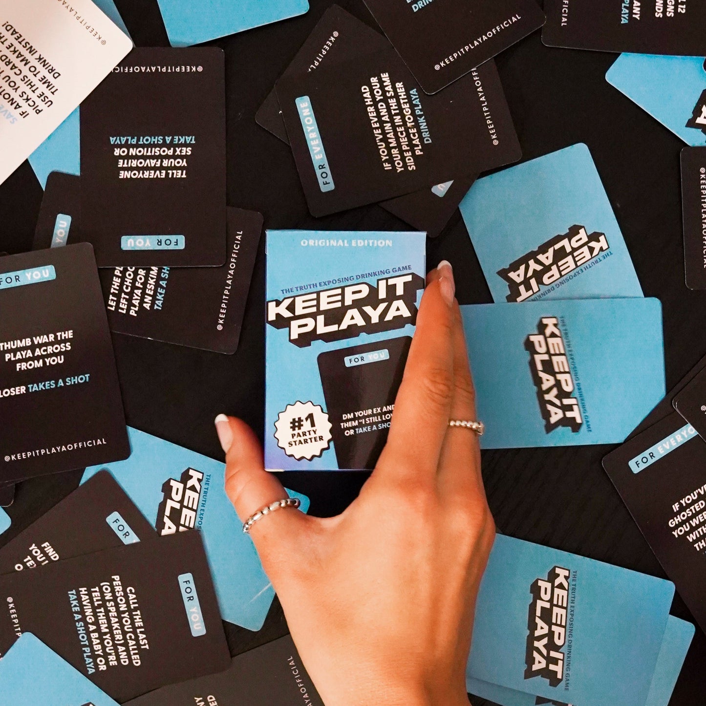 image of Keep It Playa original edition front of box being held by a hand with cards spread on table
